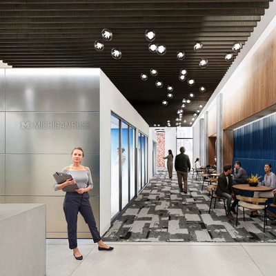 Modern office lobby with sleek design. A woman holds a laptop on the left, while people chat at tables on the right. Hanging lights and patterned carpet add style.