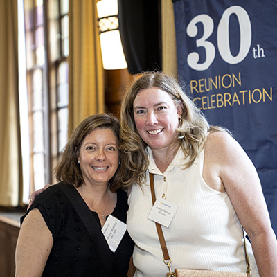2 people pose for a photo in front of 30th reunion banner