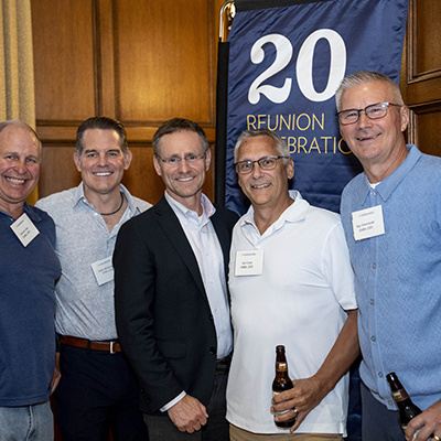 6 people pose together for a photo in front of 20th reunion banner