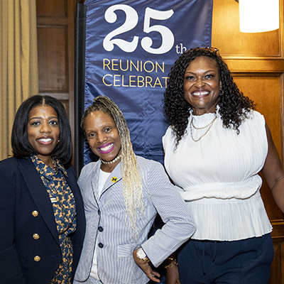 3 people pose together in front of 25th reunion banner