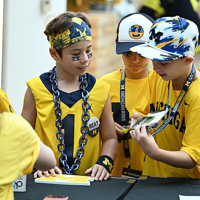 3 kids show each other their badges while wearing U of M apparel 