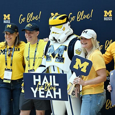 people pose with a "U of M Stormtrooper" in front of a step and shoot U of M backdrop