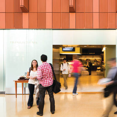 People walking in and out of a modern building lobby with a reception desk.