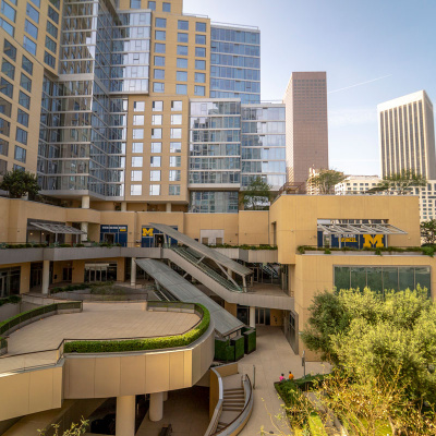 Modern multi-story university building with "M" logos and greenery in an urban setting.
