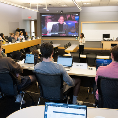 Students in a modern classroom watch a large screen as an instructor gives a lecture.