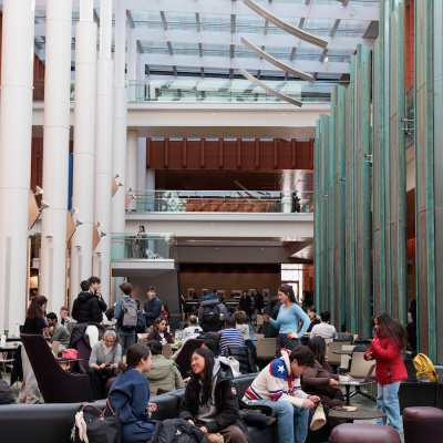Students gather and study in a bright, modern indoor common area with large windows.