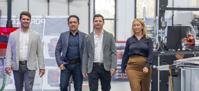 Four people in business attire walk confidently through a modern industrial facility, displaying a sense of teamwork and professionalism.
