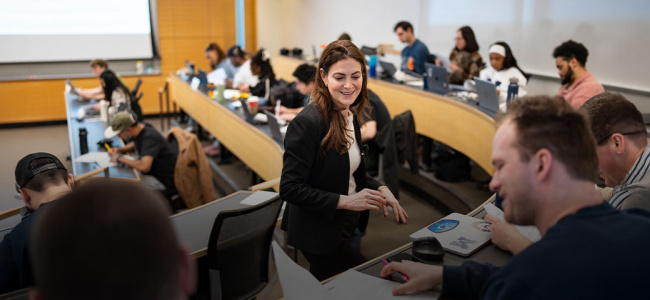 Instructor speaking with students in a tiered classroom during a discussion.