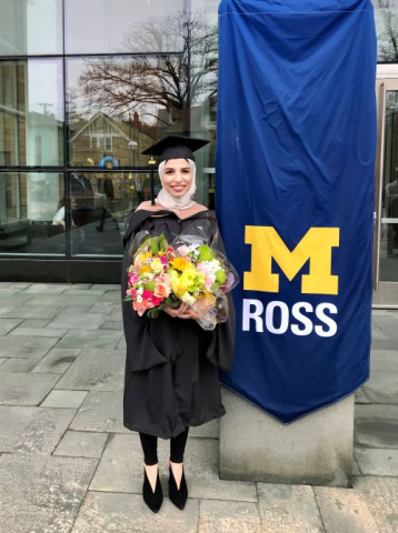 Mariam Jalloul in her cap and gown in front of a Michigan Ross banner