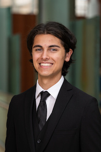Male student wearing a black suit with dark hair and smiling