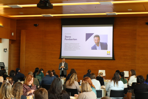 Speaker presenting to an audience with a slide displaying "Steve Pemberton" and his photo.