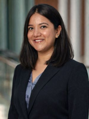 Person in a dark blazer smiling in a professional indoor setting.