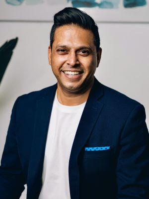 Smiling person wearing a navy blazer and white shirt in a professional setting.
