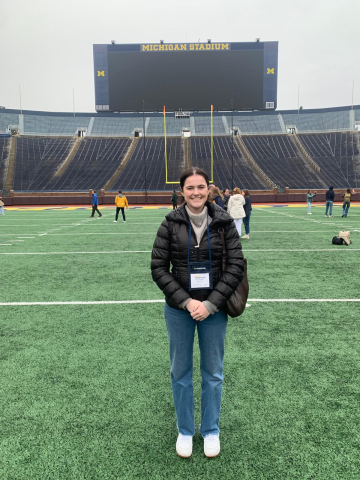 Person standing on the field at Michigan Stadium with scoreboard in the background.