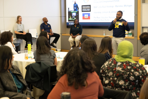 A speaker addresses an audience during a panel discussion in a conference room.