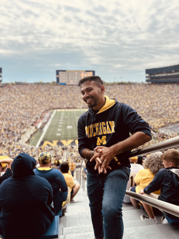 Person smiling on stadium steps during a crowded University of Michigan football game.