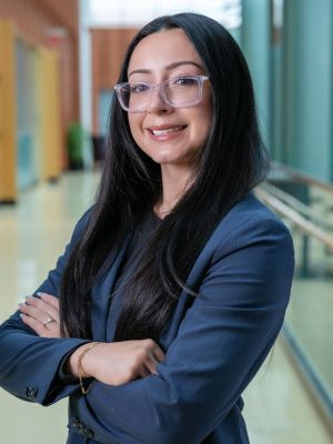 Person with long dark hair and glasses smiling in a professional indoor setting.