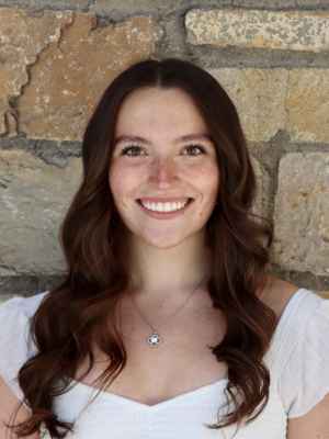 Woman with long brown hair smiling in front of a stone wall.