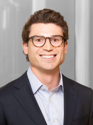 Smiling person wearing glasses and a suit in a professional setting.