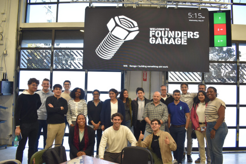 A group of people pose together inside a workspace under a "Founders Garage" event sign.