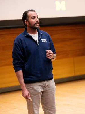 Person giving a presentation in a lecture hall with a University of Michigan logo on the screen.