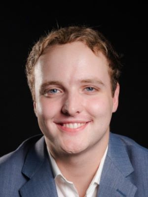 Person smiling and wearing a blue blazer against a dark background.