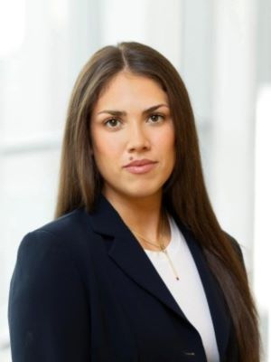 Woman with long brown hair wearing a dark blazer and white top in a professional setting.