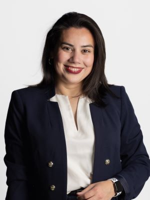Professional headshot of a smiling person wearing a navy blazer and white blouse against a light background.
