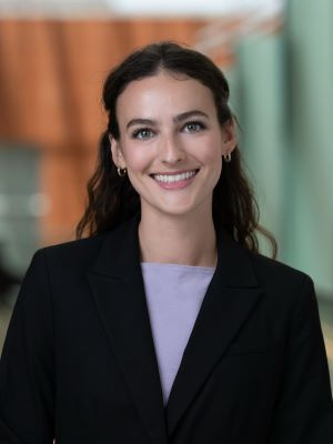 Professional headshot of a smiling woman wearing a black blazer and lavender top.