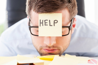 Man at desk with sticky note reading "Help" on his forehead