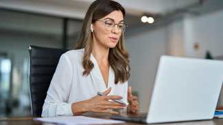 Person wearing glasses having a video call and speaking at a laptop in an office.