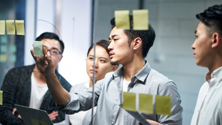 Group of colleagues brainstorming and discussing ideas using sticky notes on a glass wall.