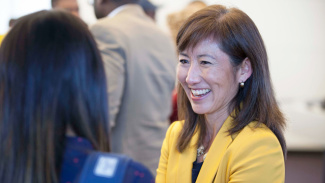 Smiling woman in a yellow blazer engages in conversation at an event.