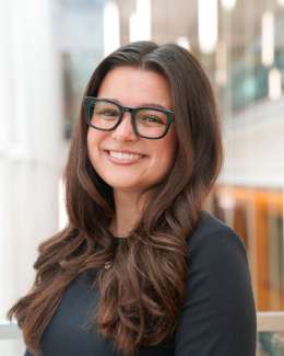 Bizzy Webb, BBA’26: Smiling person with long brown hair and black glasses in a modern indoor setting.