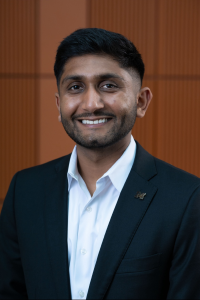 Photo of Michigan Ross Weekend MBA student Milan Patel. He is wearing a navy blue jacket with a light blue shirt. He has dark hair and dark facial hair and is smiling. 