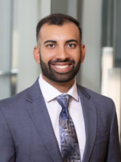 A man in a blue suit, white shirt, and blue tie smiles