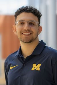 Photo of Samuel Ibri, Michigan Ross BBA student with dark curly hair and glasses, wearing a blue Michigan shirt with a maize block M