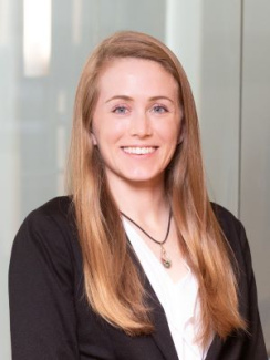 A woman with blonde hair wearing a black blazer and white shirt smiles.