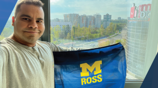 Man in front of window holding Michigan Ross flag
