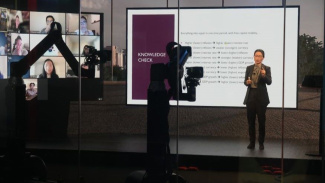 Professor standing in an online digital studio teaching to students on screen. 