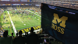 Photo of Michigan Ross flag being held up in the stands with the football field in the background