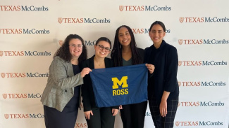 Group of four Michigan Ross BBA students holding a Michigan Ross flag in front of a backdrop at the National Women's Case Competition