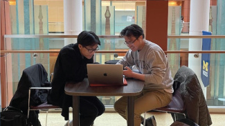 Two students sit at a table on the 2nd floor of Ross, at the open hallway/mezzanine area overlooking the Winter Garden.