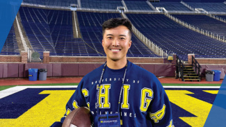 A man in a Michigan sweatshirt poses on the field in the Big House
