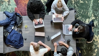 Photo of 5 students sitting in the Winter Garden at the Ross School of Business. The photo is taken from up above and is looking down onto them. They have their laptops out and they're collaborating with each other. 