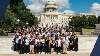 A large crowd of students stand on white steps leading up to the U.S. capitol building in Washington D.C.