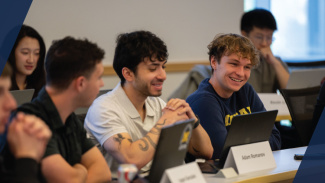 Smiling students looking at their laptops and talking during a class, sitting next to each other in a lecture hall