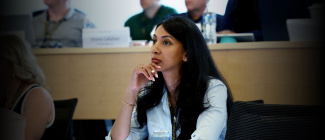 A woman attentively listens during a conference or lecture, surrounded by other focused participants. 