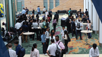 A large group of students stand in the Ross Winter Garden chatting and mingling around the tables at OYM Orientation