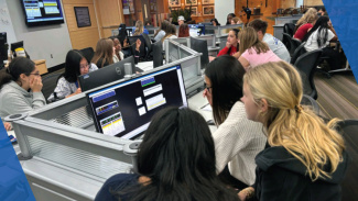 A large group of students gathers around computers in the Tozzi lab to use software like FactSet